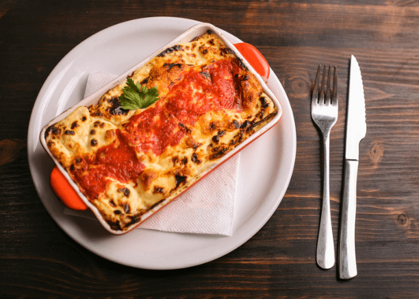 Lasagna on a white plate with silverware.