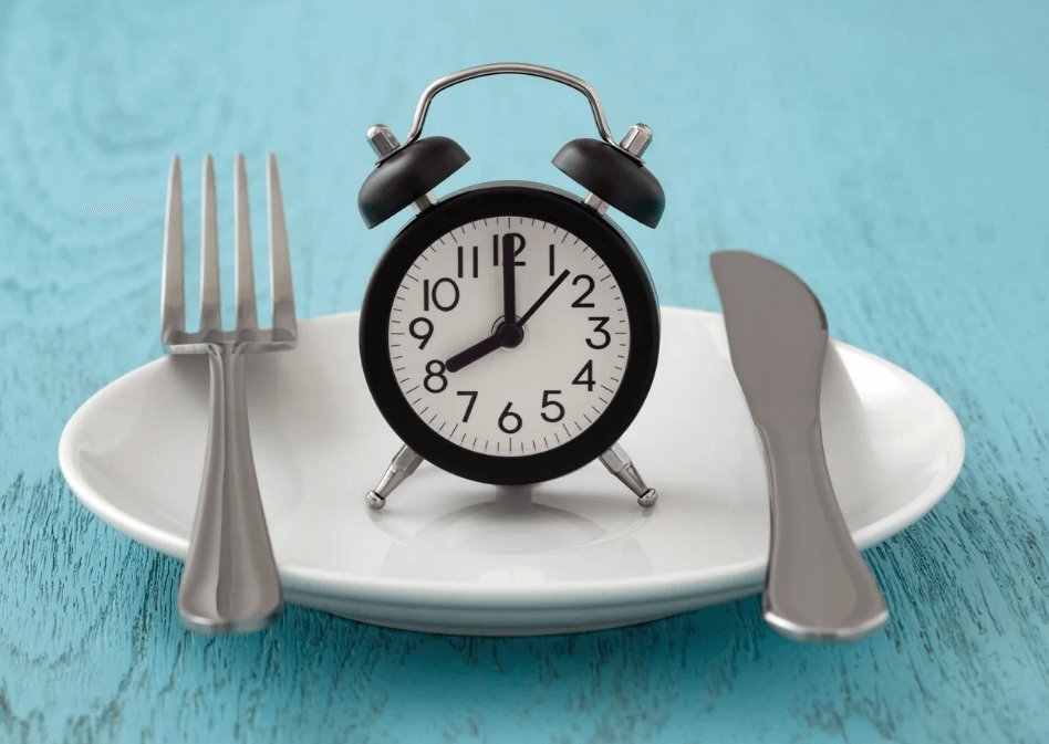 White plate with silverware and a mini black clock resting on top.