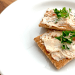 Cream cheese spread on crackers on a white plate.