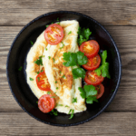 Omelet with sliced tomatoes and spinach on a black plate.