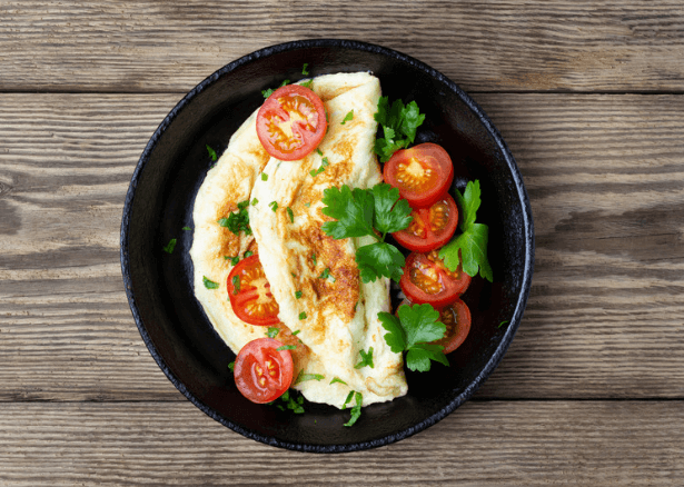 Omelet with sliced tomatoes and spinach on a black plate.