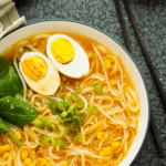 A bowl of vegetable ramen noodles garnished with a boiled egg cut in half lengthwise and a small bunch of leafy greens