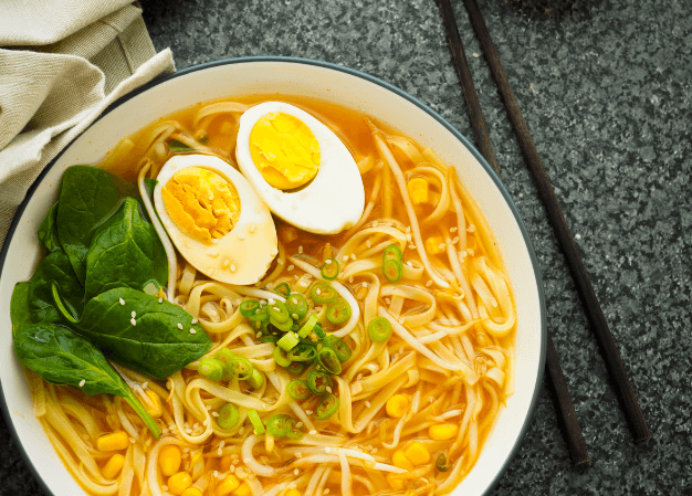 A bowl of vegetable ramen noodles garnished with a boiled egg cut in half lengthwise and a small bunch of leafy greens