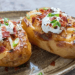 Two baked potatoes topped with cheese, sour cream, bacon, and chopped green onions