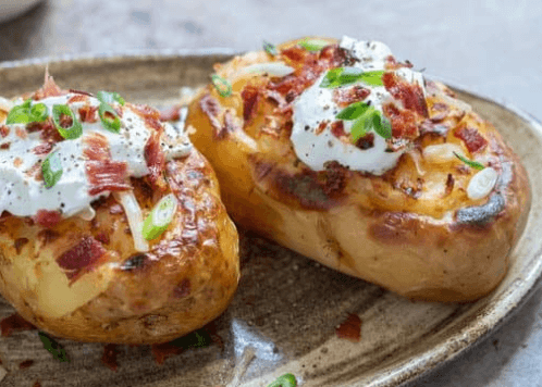 Two baked potatoes topped with cheese, sour cream, bacon, and chopped green onions