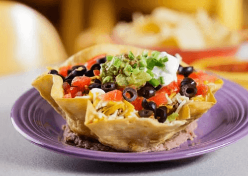 A taco salad in a bowl made from a tortilla on a purple plate