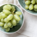Two teal bowls of green grapes on a white tea towel