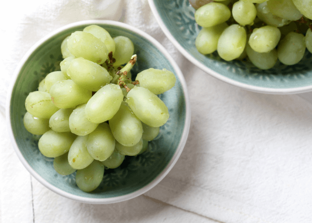 Two teal bowls of green grapes on a white tea towel