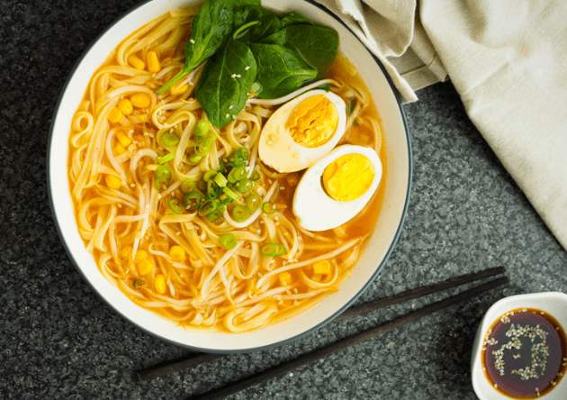 A bowl of vegetable ramen noodles garnished with a boiled egg cut in half lengthwise and a small bunch of leafy greens