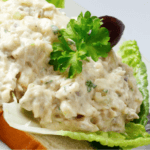 A closeup of a salmon salad on top of a large piece of lettuce and a slice of bread