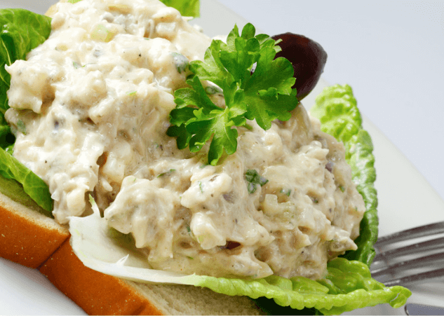 A closeup of a salmon salad on top of a large piece of lettuce and a slice of bread