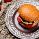 An overhead photo of a black bean burger with tomato and smashed avocado on a wheat bun
