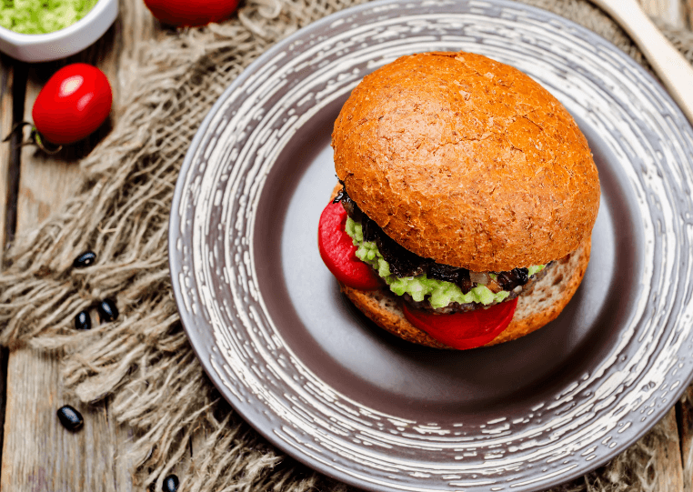 An overhead photo of a black bean burger with tomato and smashed avocado on a wheat bun