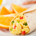 A closeup photo of a breakfast burrito with egg and red and green peppers