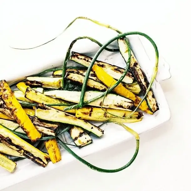 Grilled zucchini and garlic scapes on a white serving tray