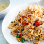 Fried rice with peas, carrots, and eggs on a white plate.