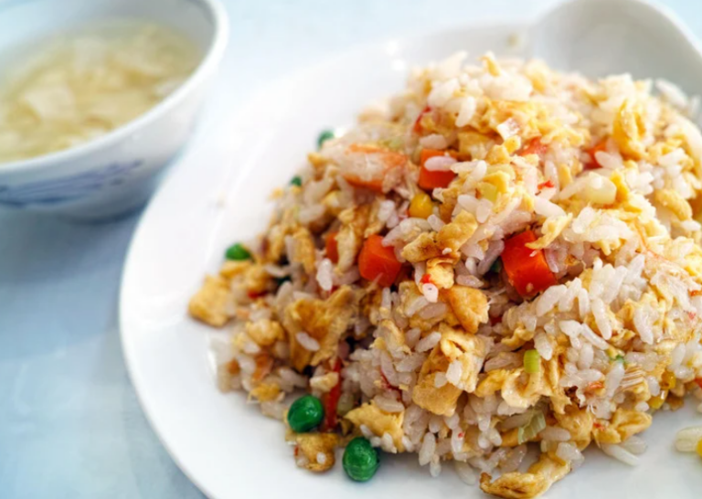 Fried rice with peas, carrots, and eggs on a white plate.