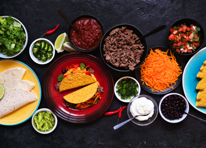 Taco shells, ground beef, guacamole, sour cream, and other taco ingredients on a black surface.