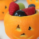 Orange cut into a jack o lantern with mixed fruit.