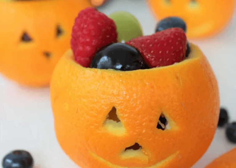 Orange cut into a jack o lantern with mixed fruit.