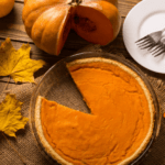 Pumpkin pie with a slice cut out, leaves, and pumpkin