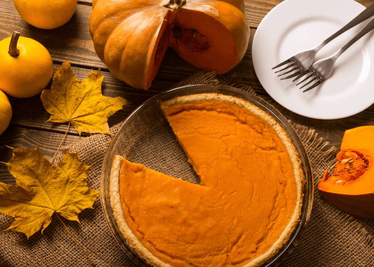 Pumpkin pie with a slice cut out, leaves, and pumpkin