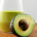 Green colored milkshake with half an avocado with put inside