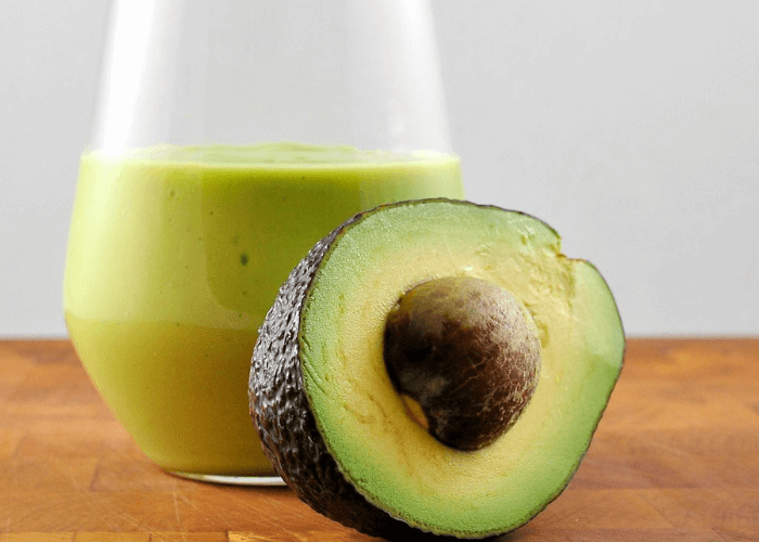 Green colored milkshake with half an avocado with put inside