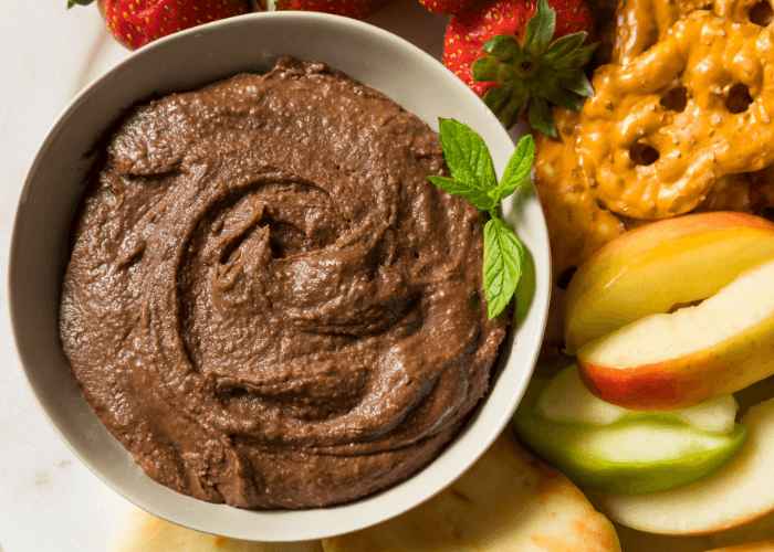 Chocolate Hummus served in a bowl with sliced apples and pretzels