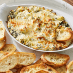 Hot Spinach Artichoke Dip in a white dish with slices of bread