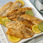 Pan-Seared Tilapia fillets, lemons, and limes on a white plate