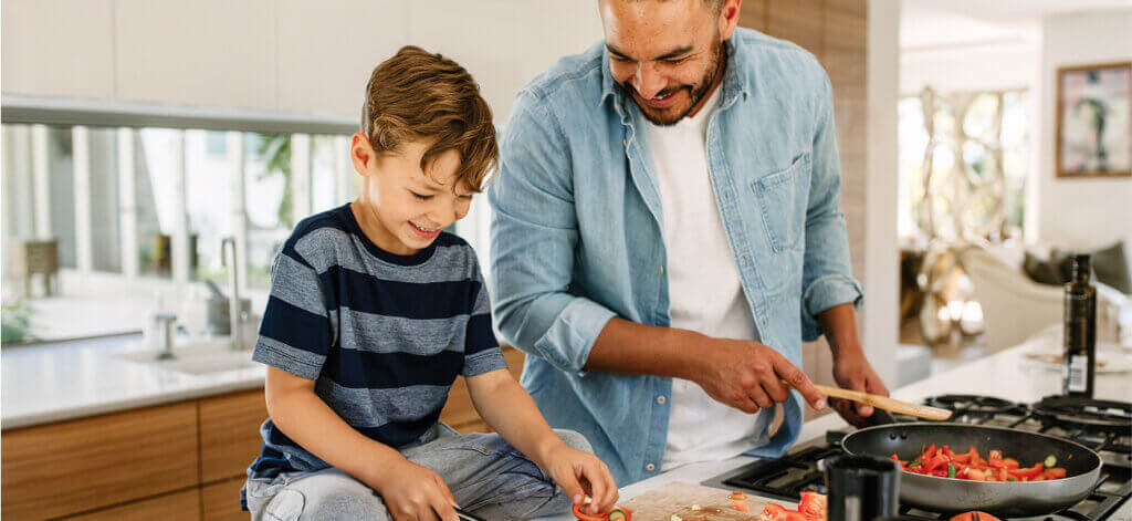 A boy sitting on the counter with his father cooking together